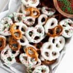White Chocolate Pretzels with red and green sprinkles piled on parchment paper.