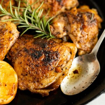 crispy chicken thighs in a cast iron pan with fresh rosemary and a silver spoon.