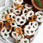 white chocolate covered pretzels with Christmas sprinkles on a parchment lined baking sheet.