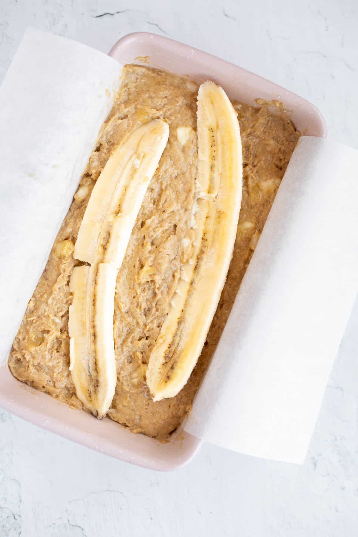 easy banana bread batter in a pink loaf pan topped with half a banana.
