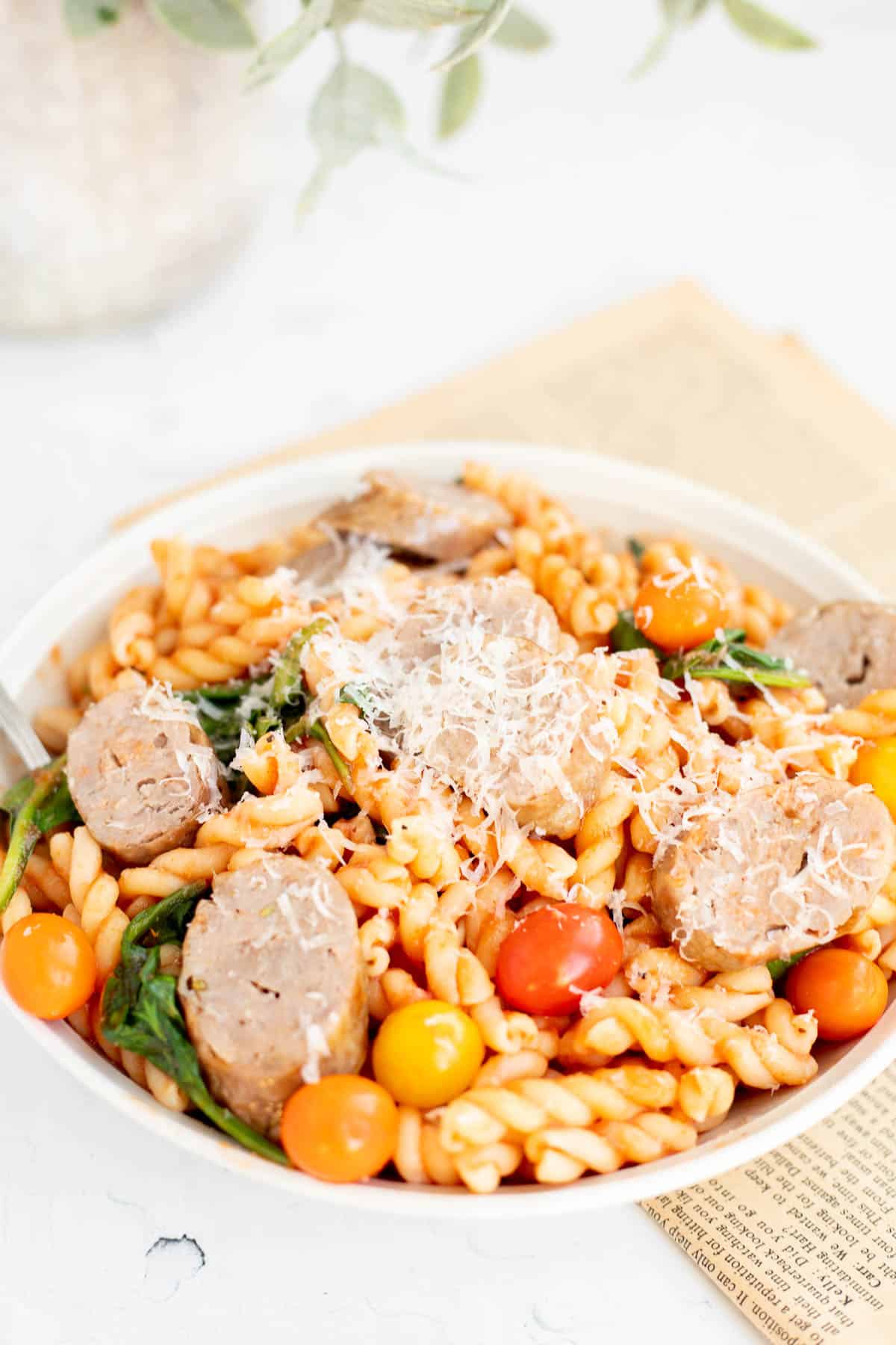 air fryer Italian sausage mixed with pasta, spinach, and tomatoes, in a white bowl.