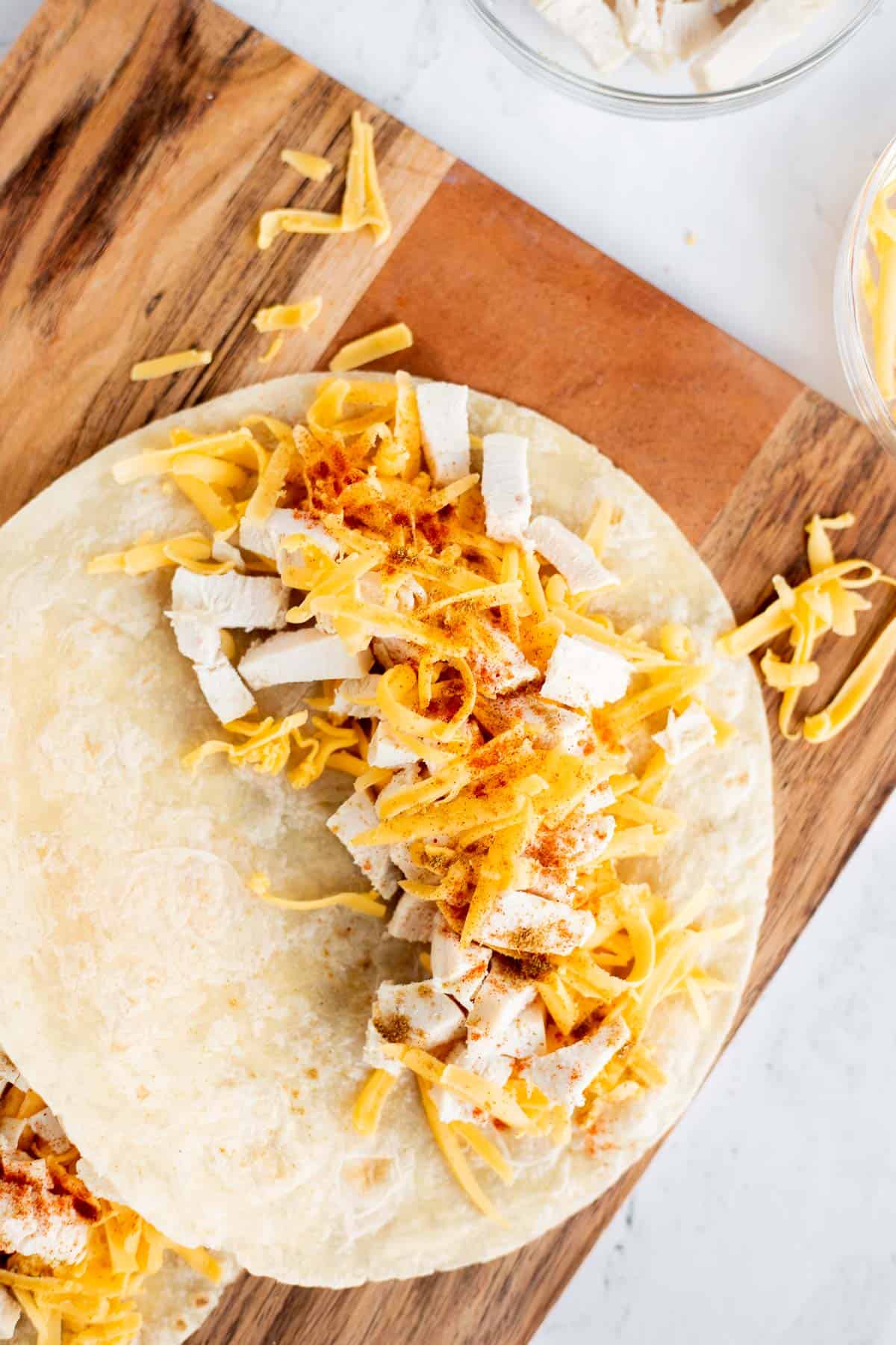 flour tortilla with half covered in shredded cheese and diced chicken.