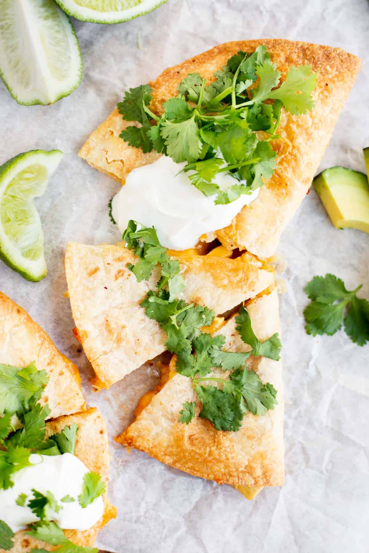 cheese quesadilla cut into triangles on parchment paper and topped with cilantro and sour cream.