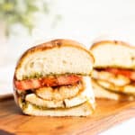 chicken caprese sandwich cut in half on a wooden board facing the camera.