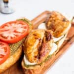 open faced chicken caprese sandwich on a wooden cutting board.