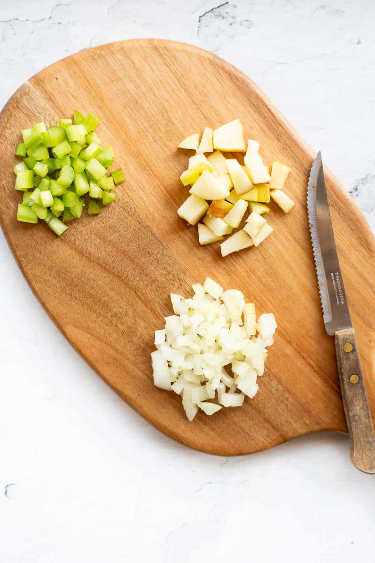 chopped celery, onions, and apples on a wooden cutting board.