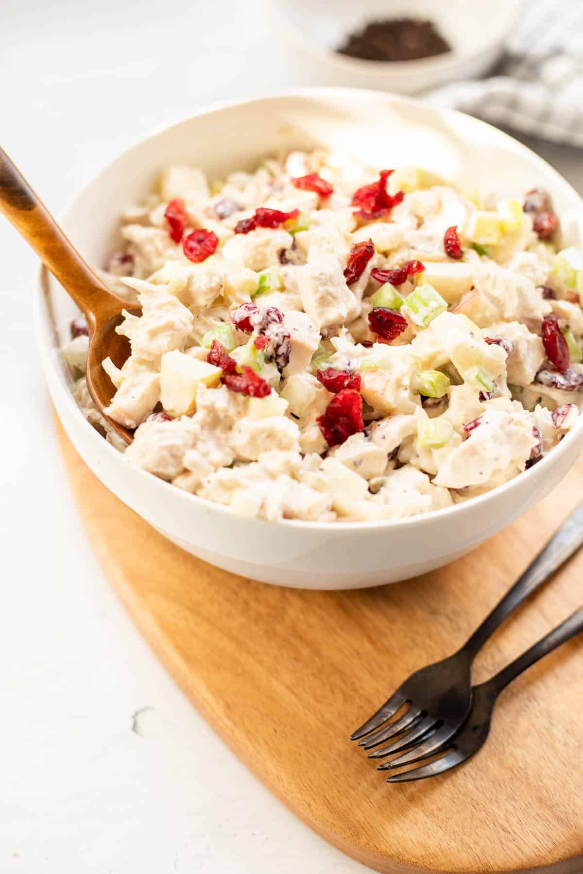 chicken salad with cranberries in a white bowl with a wooden serving spoon.