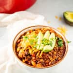 white bowl of Dutch oven chili topped with avocado and cheese.