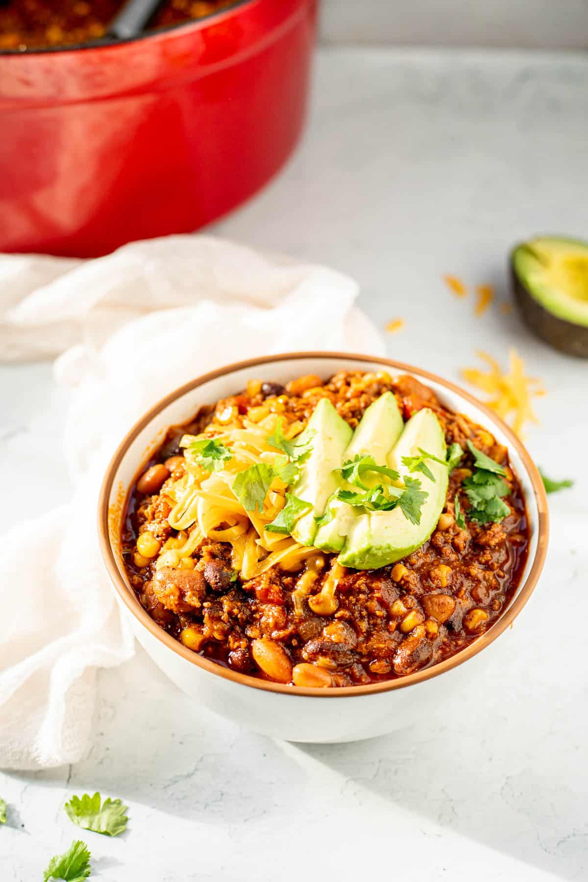 white bowl of Dutch oven chili topped with avocado and cheese.