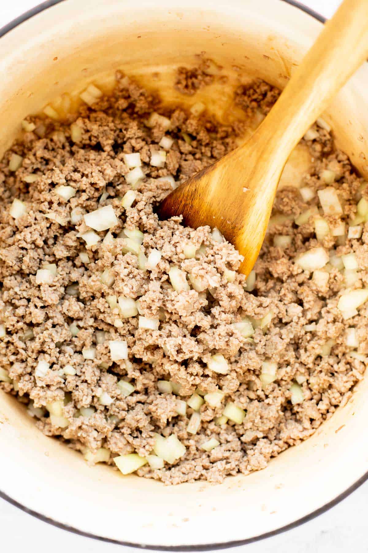browned ground meat with diced onion in a pot with a wooden spoon.