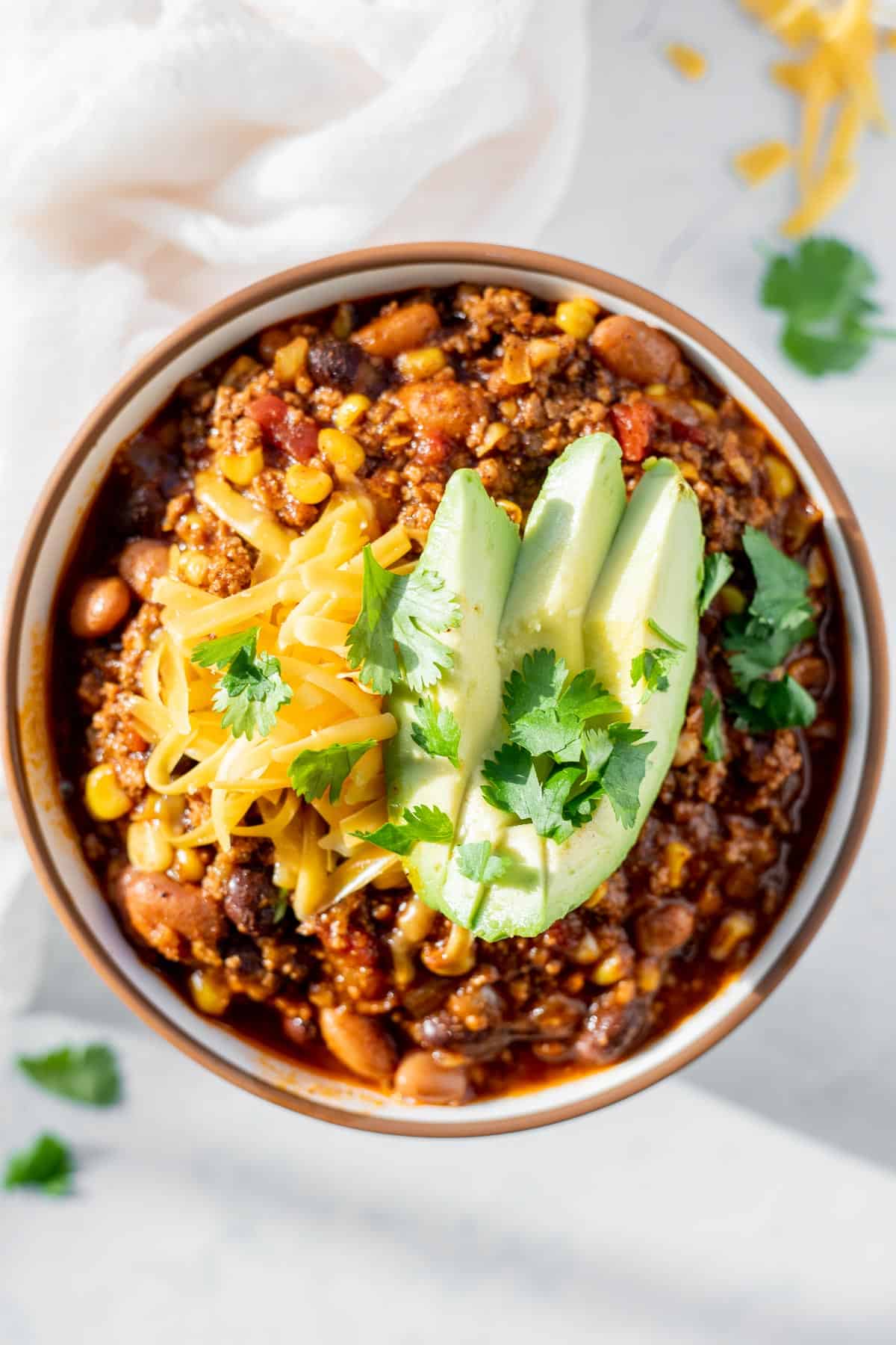 stovetop chili in a white bowl topped with avocado and shredded cheese.