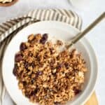 healthy granola in a white bowl with a gold spoon on a wooden board.