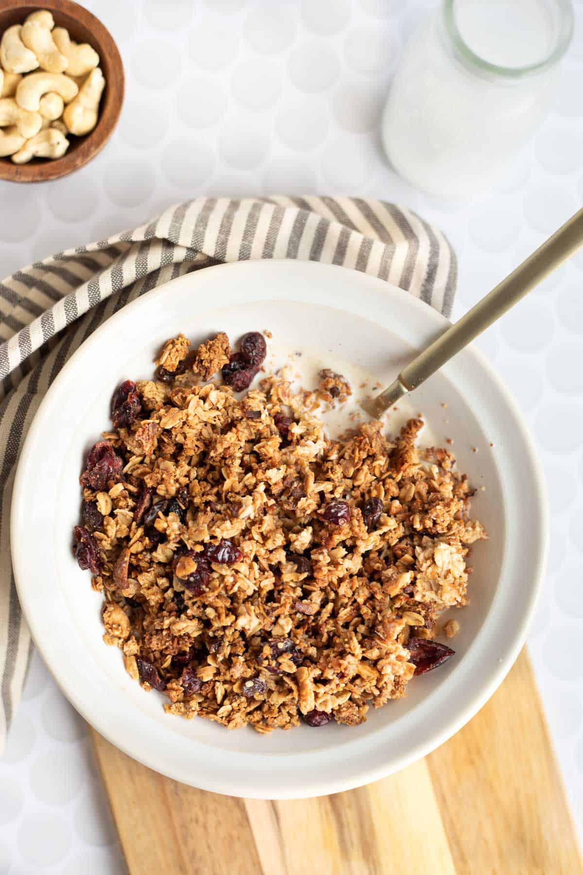 healthy granola in a white bowl with a gold spoon on a wooden board.