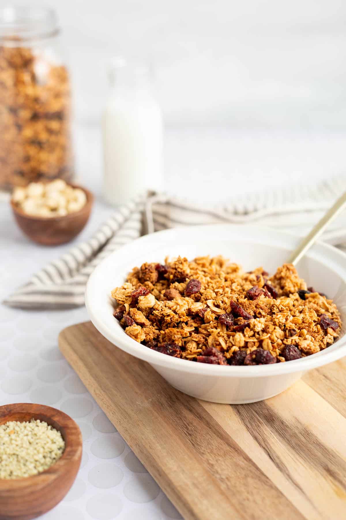 a large white bowl of vegan and gluten free granola on a wood board with jars in the background.