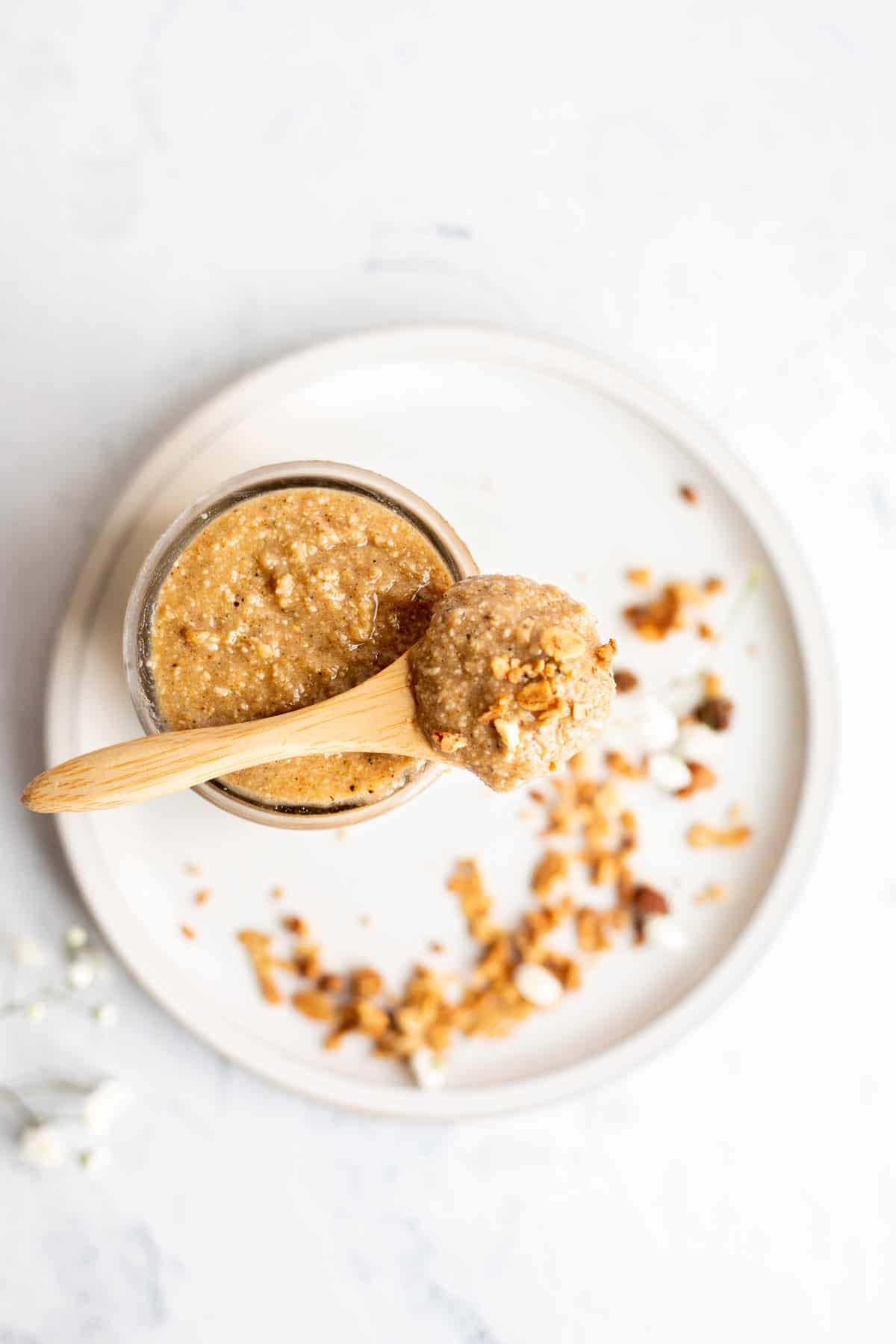 granola butter on a small wooden spoon resting on a glass jar sitting on a white plate.