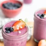 Greek yogurt smoothie in a glass jar topped with strawberry half , blueberries, and white flowers.