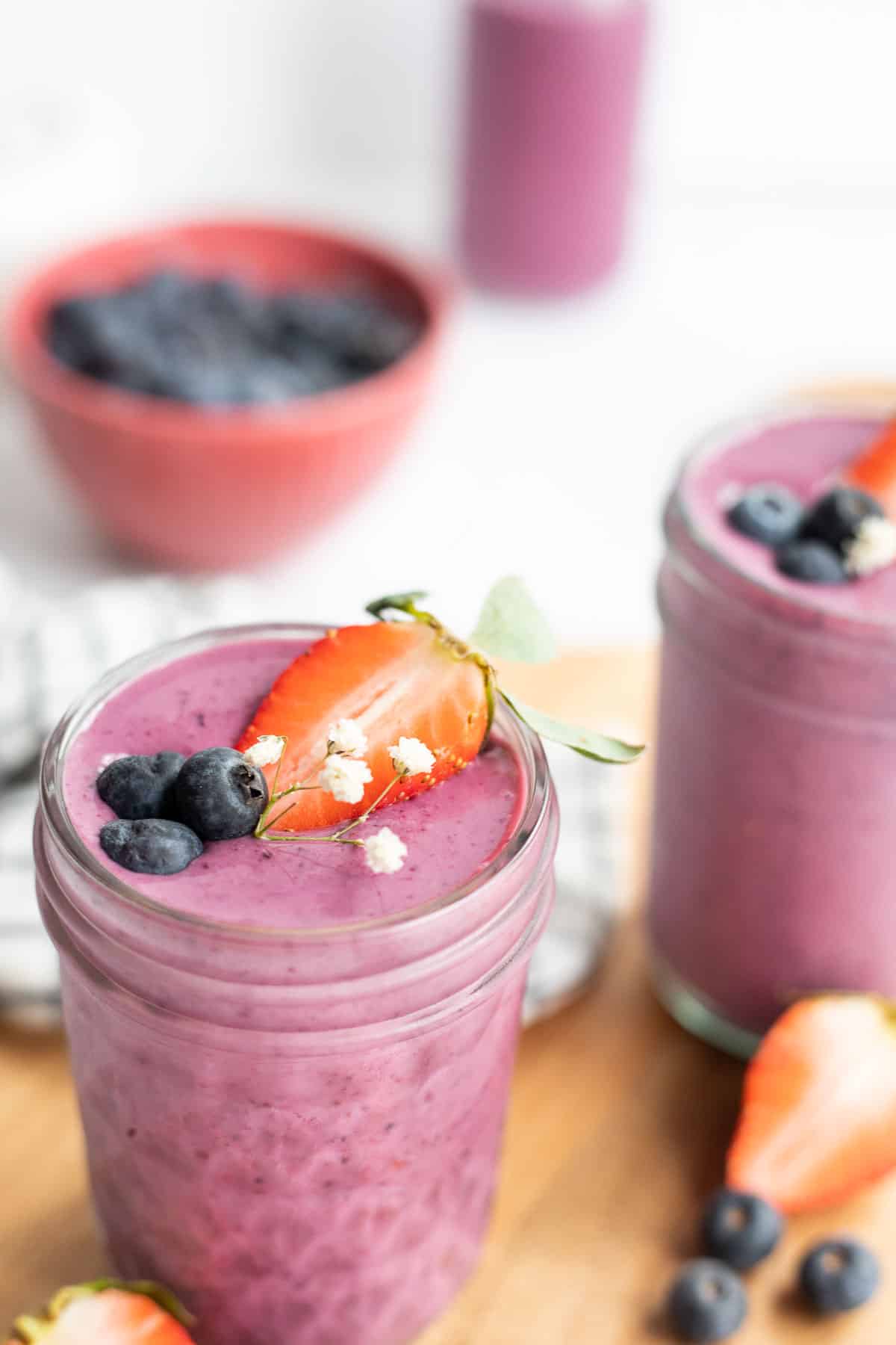 Greek yogurt smoothie in a glass jar topped with strawberry half , blueberries, and white flowers.
