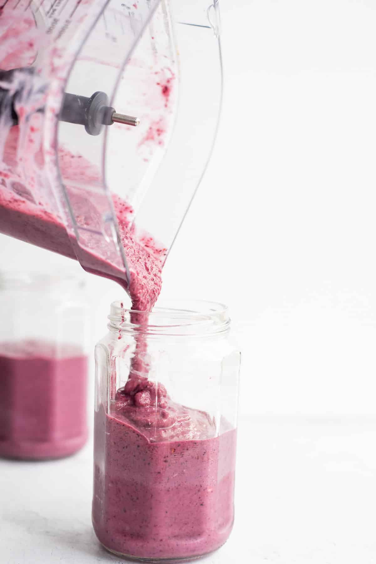 mixed berry smoothie pouring from a blender into a glass jar.
