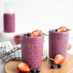 two berry yogurt smoothies in glass jars topped with fresh berries on a wooden board.