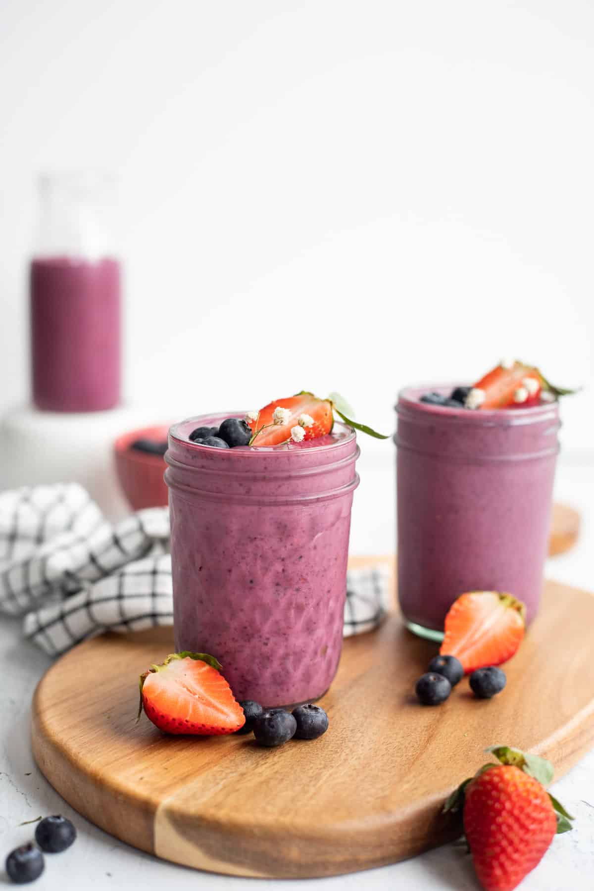two berry yogurt smoothies in glass jars topped with fresh berries on a wooden board.