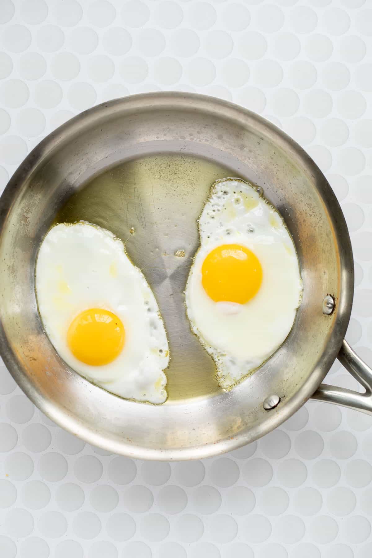 two sunny side up eggs in a stainless steel pan.