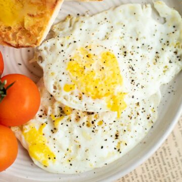 2 over hard eggs on a white plate with tomatoes and buttered bread,
