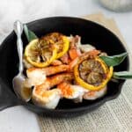 pan seared shrimp in a cast iron pan with fresh sage, a silver spoon, and seared lemon slices.