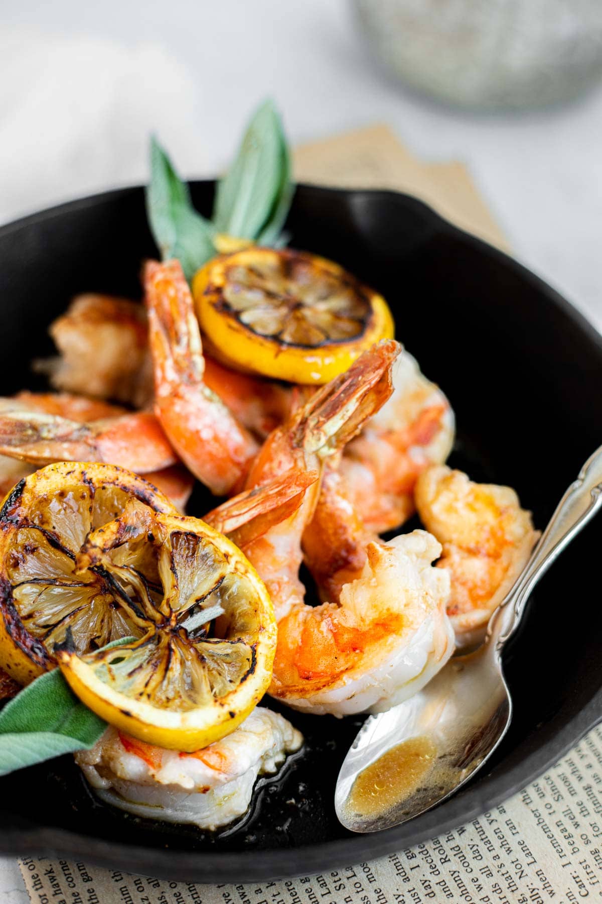 pan seared shrimp in a cast iron skillet with lemon slices and sage leaves.