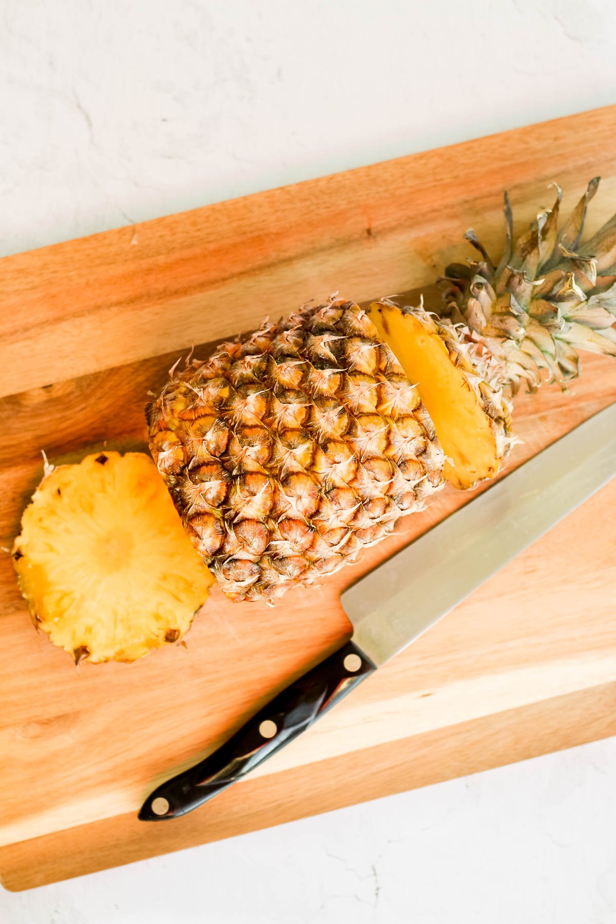 pineapple on a cutting board with the top and bottom chopped off.