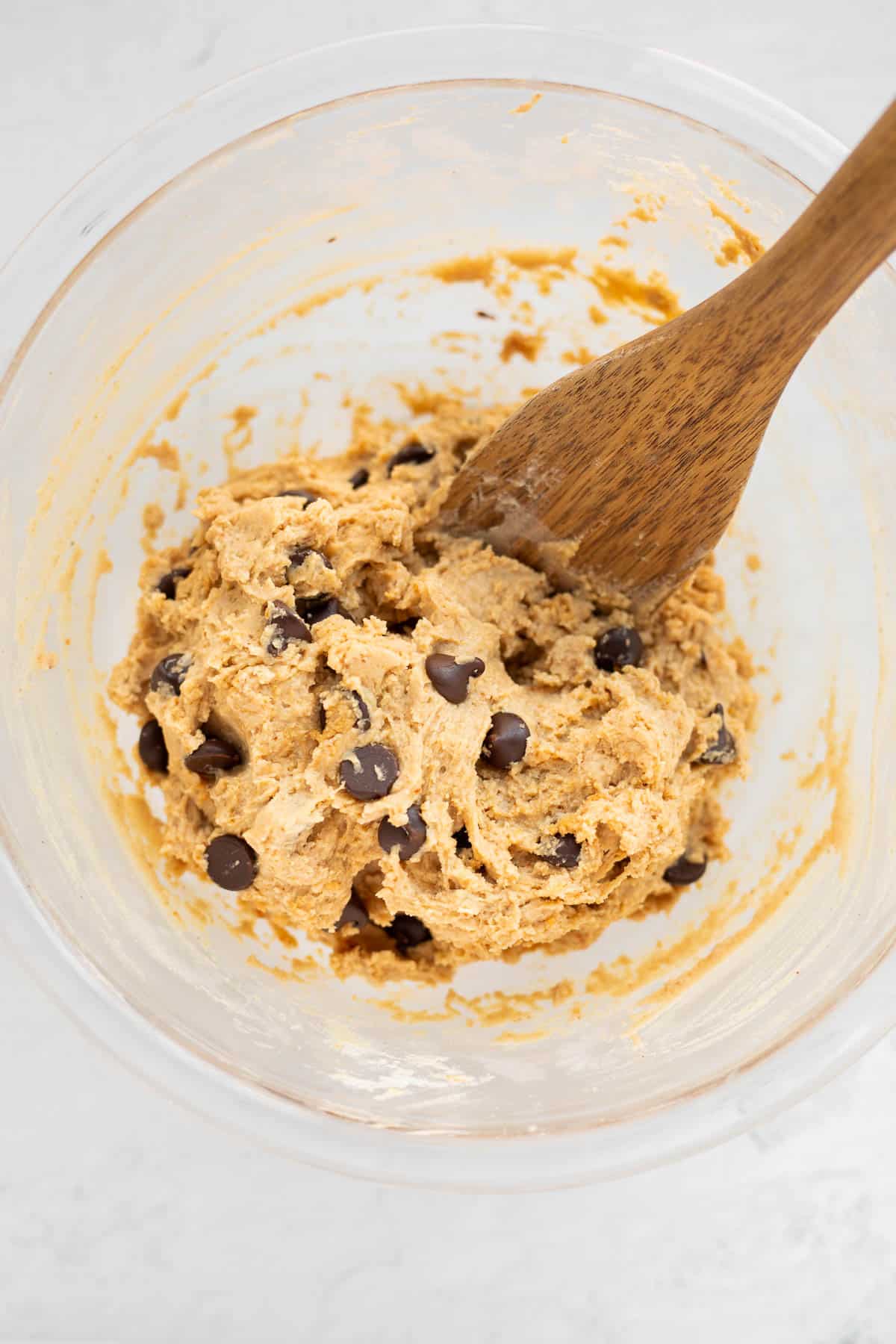 edible cookie dough with protein in a glass bowl with a wooden spoon.
