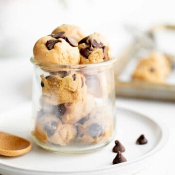 balls of edible cookie dough with chocolate chips in a glass jar on a white plate.