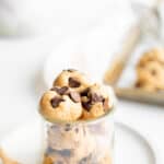 balls of edible cookie dough with chocolate chips in a glass jar on a white plate.