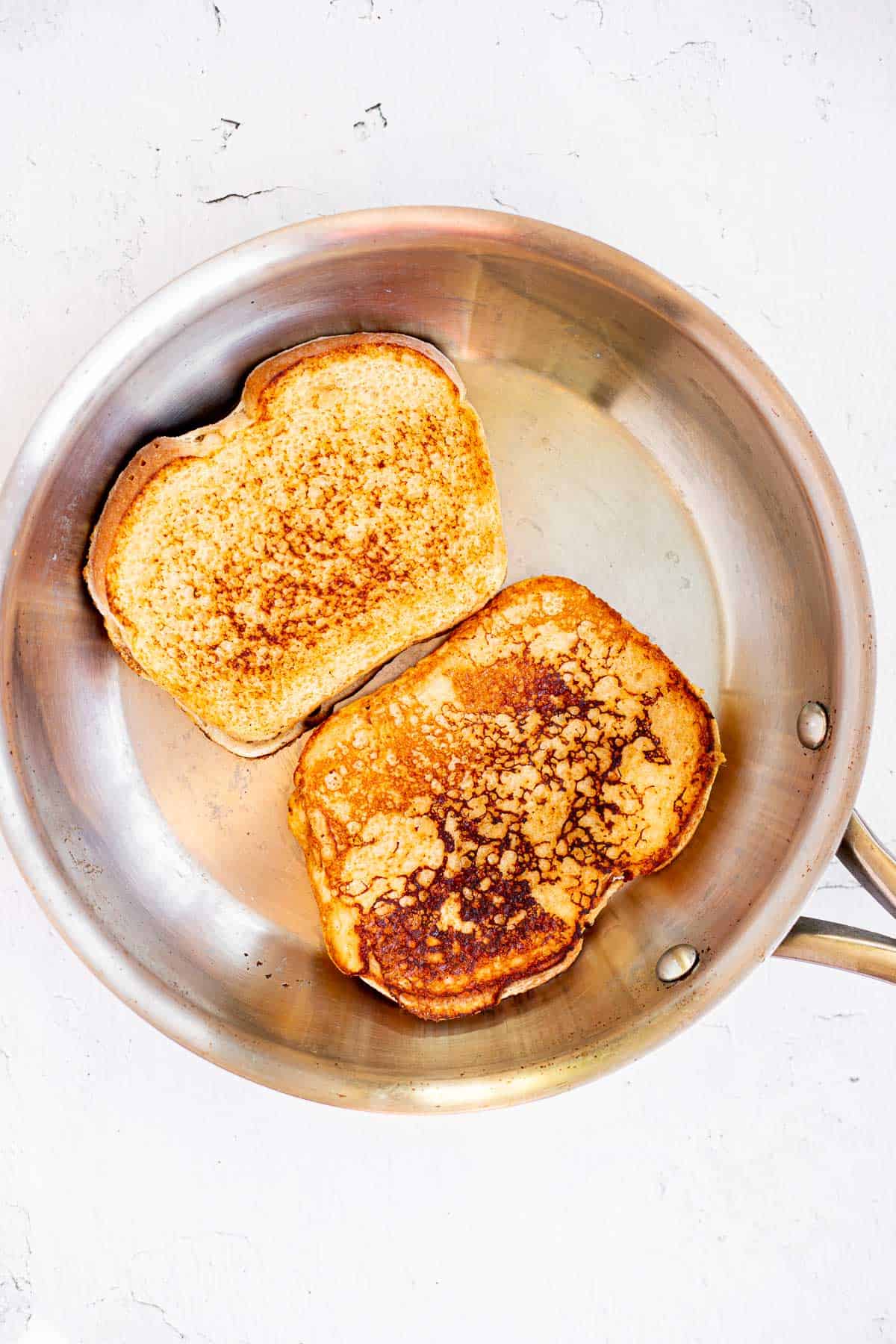 two slices of golden brown protein French toast cooked in a stainless steel plan.