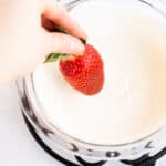 hand dipping a strawberry into melted white chocolate.