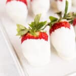 white chocolate covered strawberries on a parchment lined baking sheet.