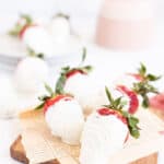 strawberries dipped in white chocolate on a wooden board lined with newspaper.