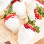 white chocolate covered strawberries on a paper lined wooden board.
