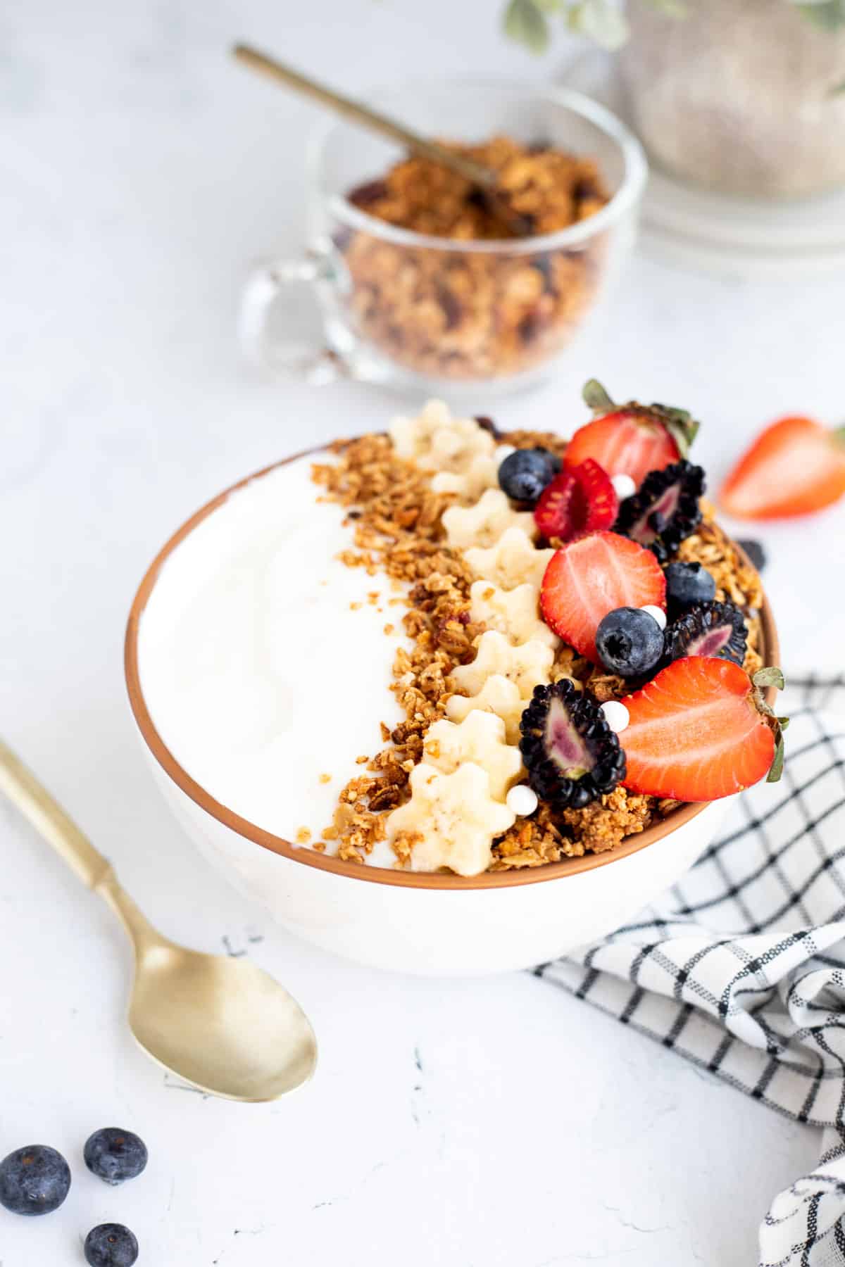 white bowl of yogurt with granola, mixed berries, and bananas.