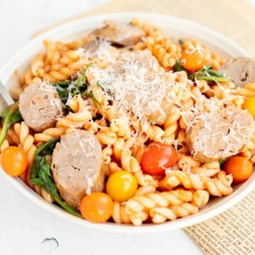 air fryer Italian sausage mixed with pasta, spinach, and tomatoes, in a white bowl.
