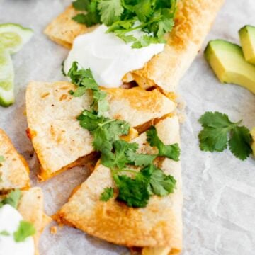 air fryer quesadilla cut into triangles with cilantro and sour cream on top.