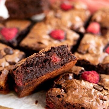 1 raspberry brownie leaning on another brownie on parchment paper.