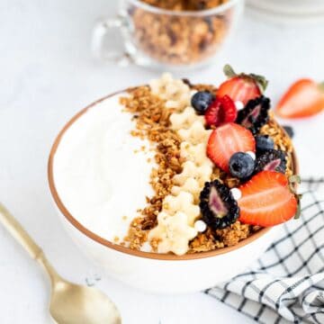 white bowl of yogurt with granola, sliced of banana, and mixed berries.