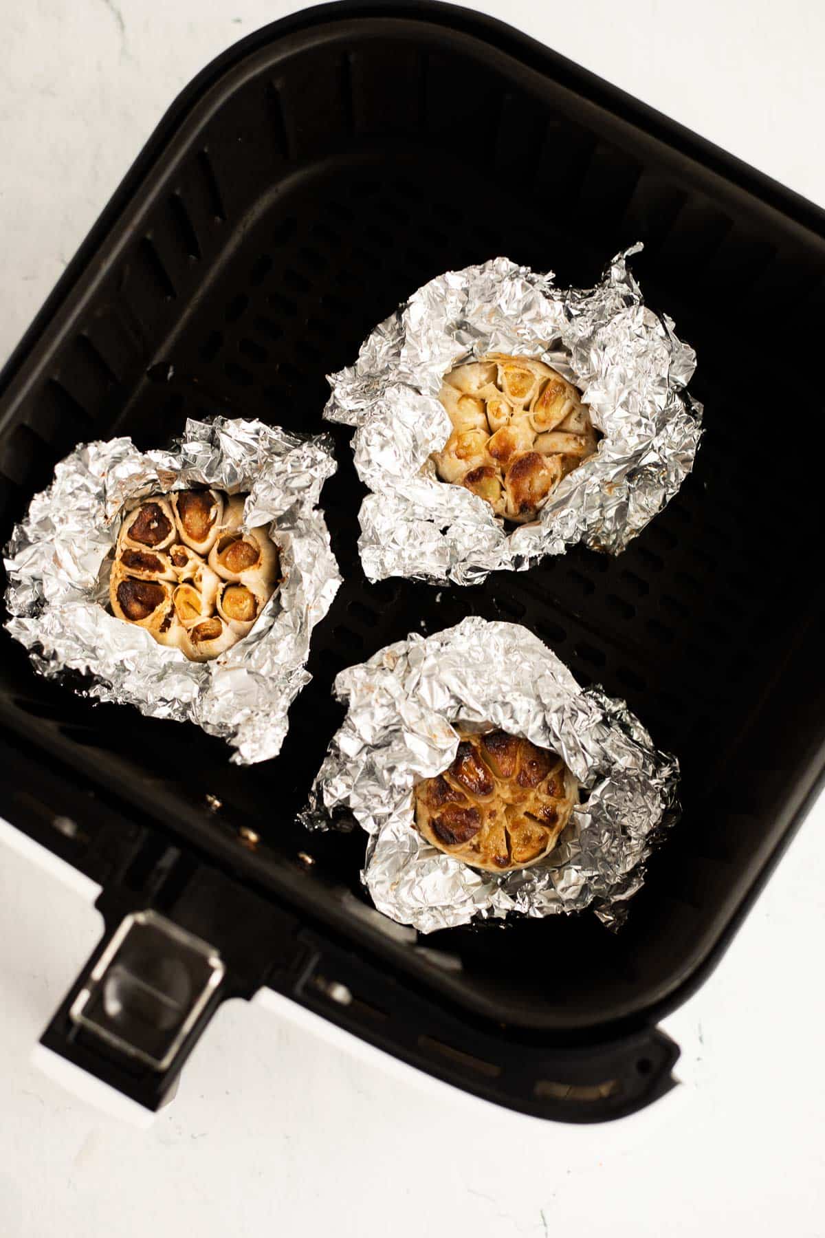 3 bulbs of garlic in aluminum foil roasted in an air fryer basket.