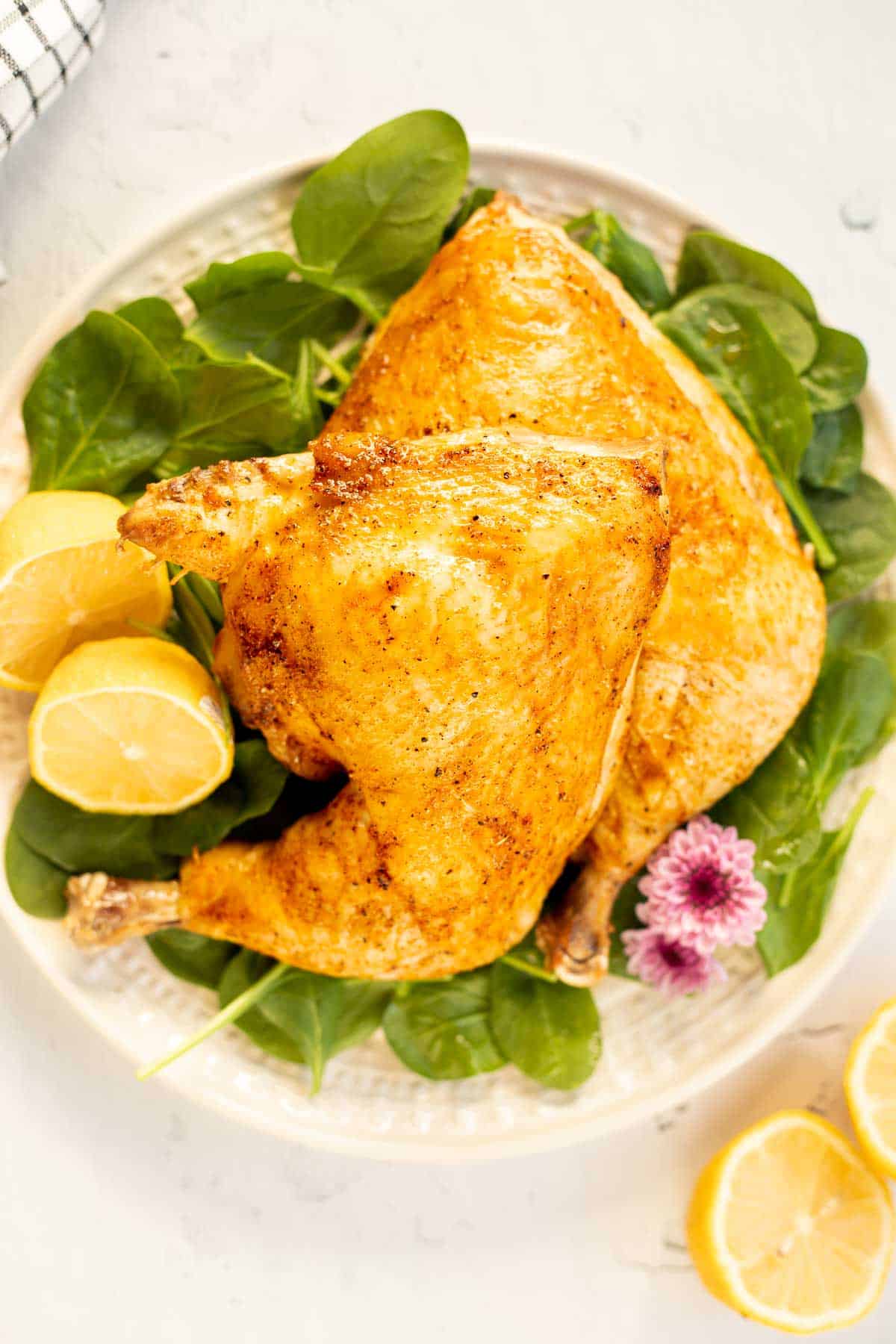 baked chicken quarters on a white plate with spinach and lemon halves.
