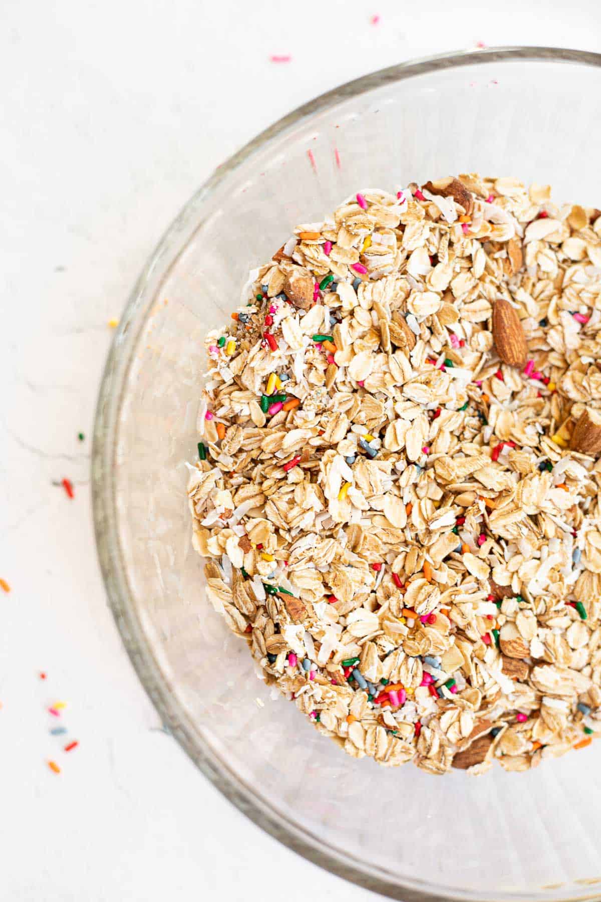 oats, almonds, sprinkles, and coconut in a glass bowl.
