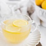a clear mug of hot honey lemon water on a white plate.