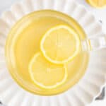 2 thin lemon slices floating in a clear mug of honey lemon tea.