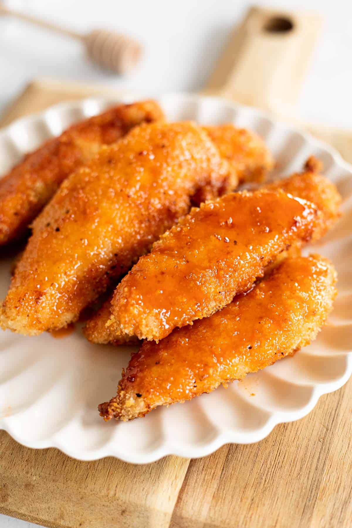 a pile of hot honey chicken tenders on a white plate with scalloped edges.