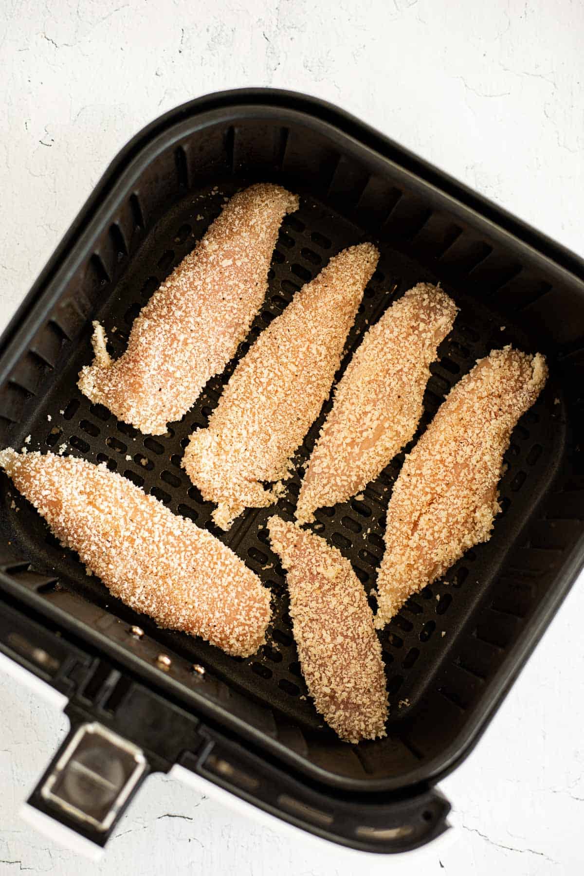 breaded chicken tenders in air fryer basket.