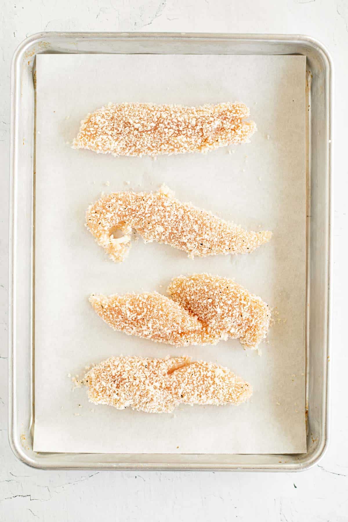 breaded chicken strips on parchment lined baking sheet.